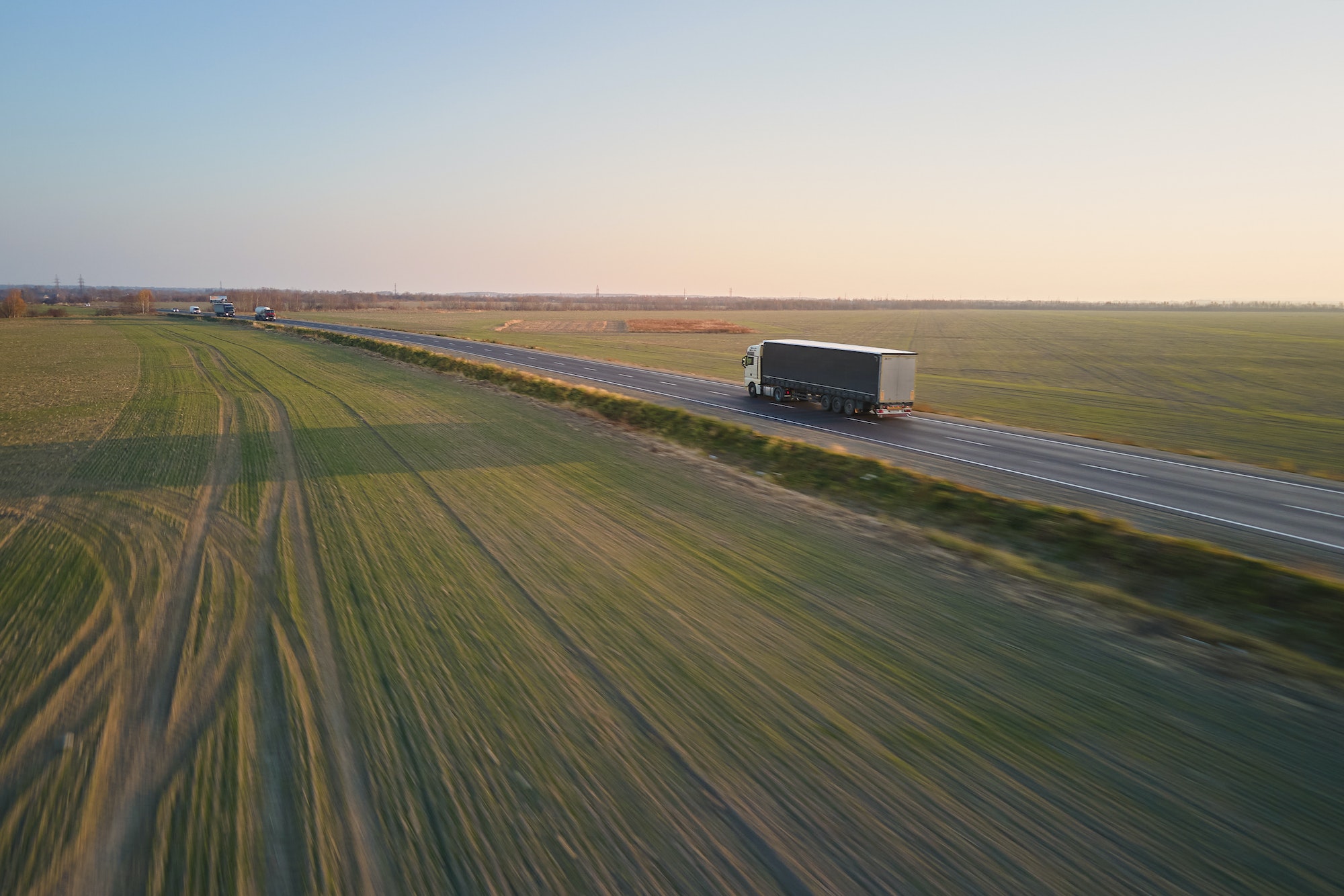 Aerial view of semi-truck with cargo trailer driving on highway hauling goods in evening. Delivery