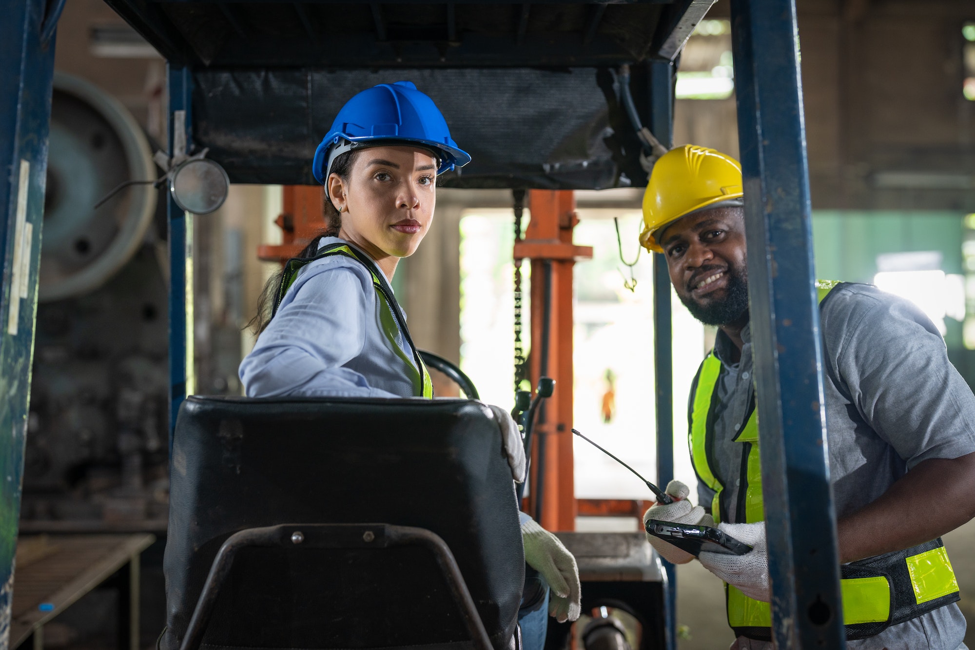 African American female worker driving forklift truck in heavy metal industrial factory