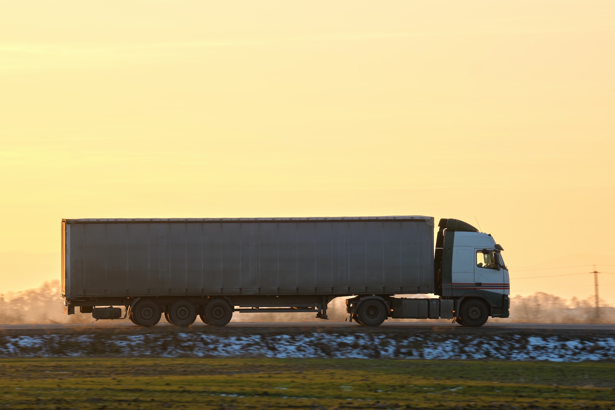 Semi-truck with cargo trailer driving on highway hauling goods in evening