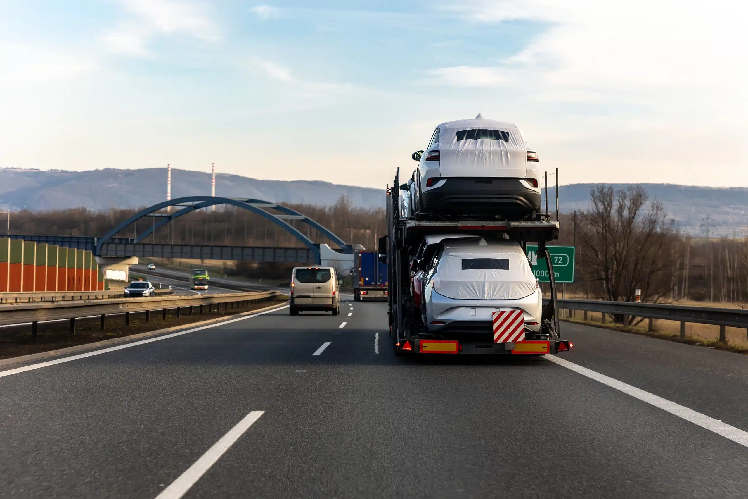Tow truck car carrier semi trailer on highway carrying batch of new wrapped electric SUVs on